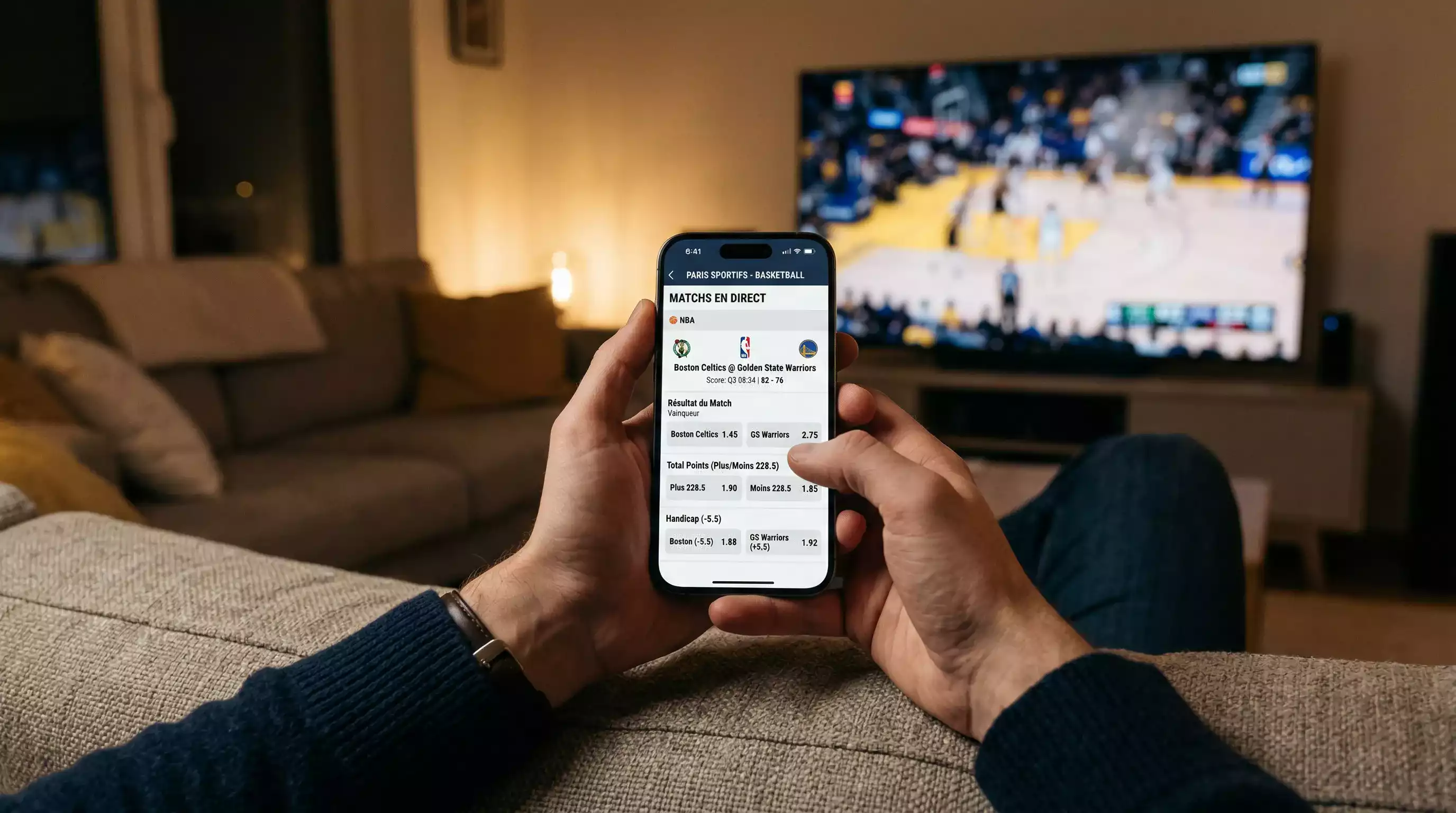 Personne consultant une application de paris sportifs sur smartphone avec match de basketball en arrière-plan